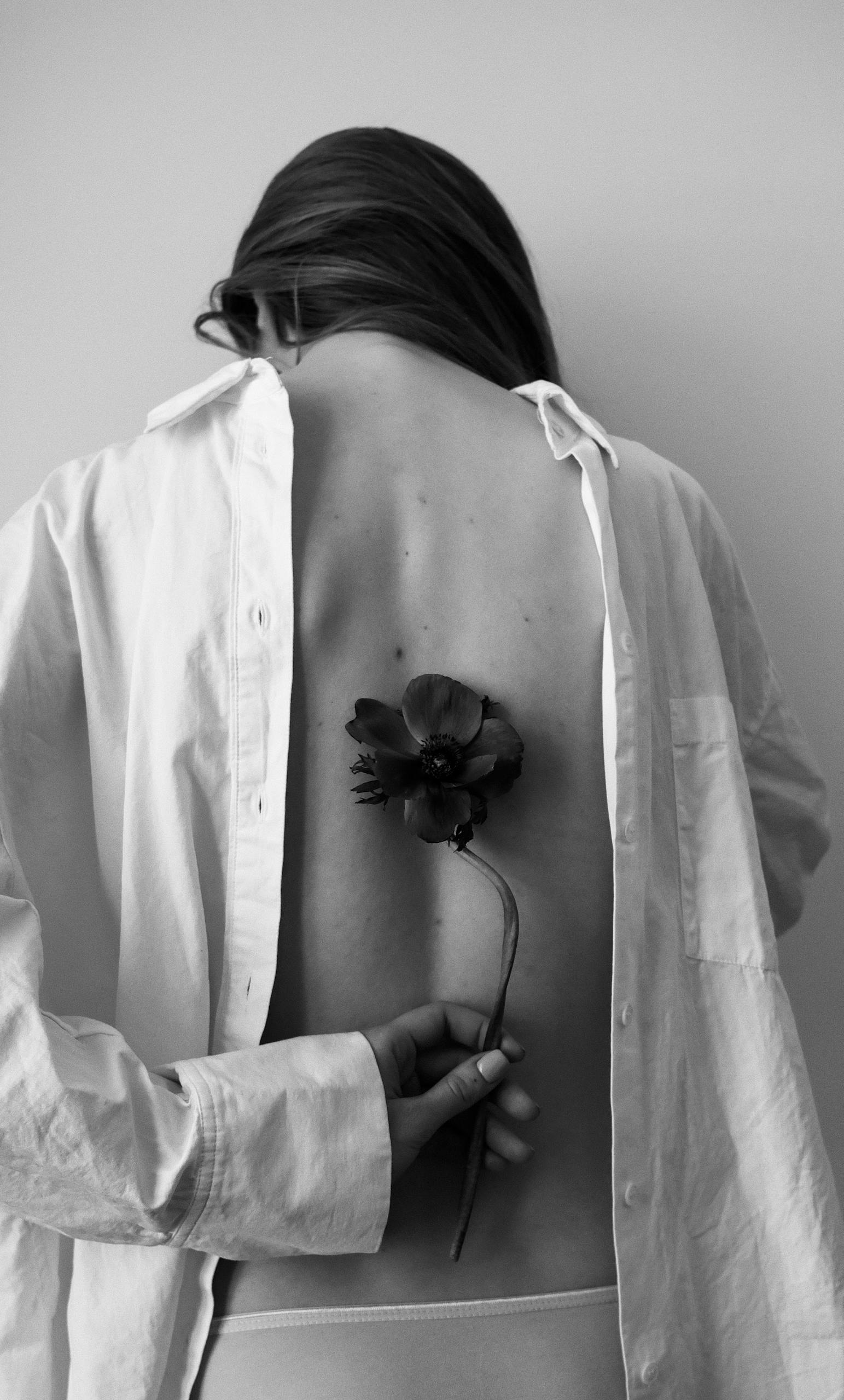 Monochrome image of a woman holding a flower behind her back, artistically posed.